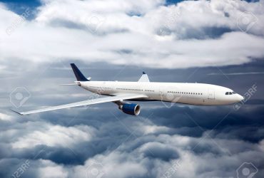 Side view of white aircraft in flight. The passenger plane flies Side view of white aircraft in flight. The passenger plane flies high between the clouds layers.